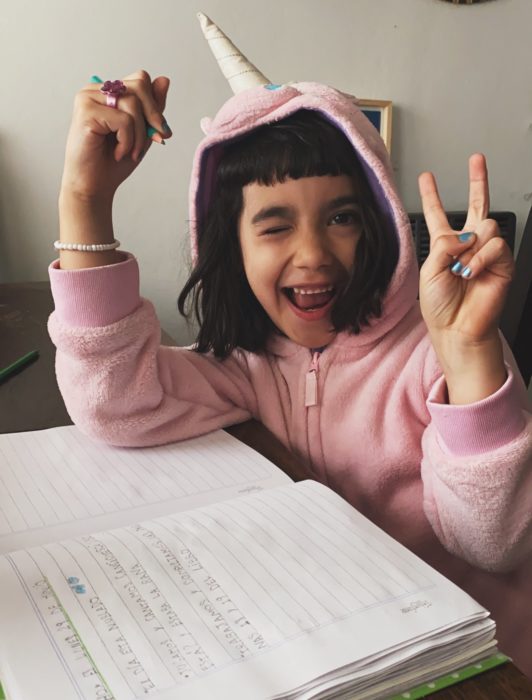 Niña llamada Agostina usando una sudadera de unicornio mientras hace su tarea