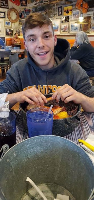 Chico de 17 años, con sudadera gris, comiendo pizza y sonriendo en un restaurante