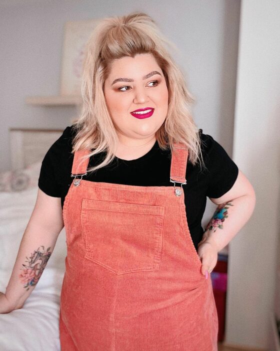Priscila Arias la influencer llamada Fatshionista posando para una fotografía mientras usa un jomper de color coral con una blusa negra