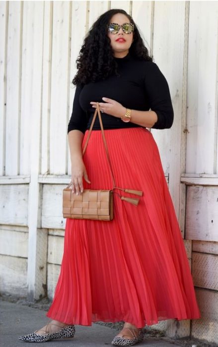 chica con falda plisada coral y blusa negra de manga larga
