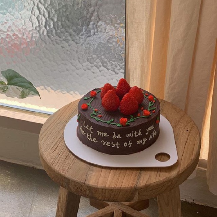 Pastel de la repostera Koike, de chocolate, con fresas y rosas pequeñas, además de una frase en color blanco