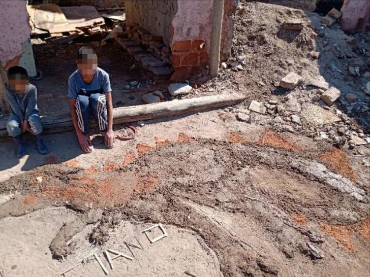 Niños sentados a la orilla de una puerta haciendo figuras de dinosaurio con barro y ladrillos