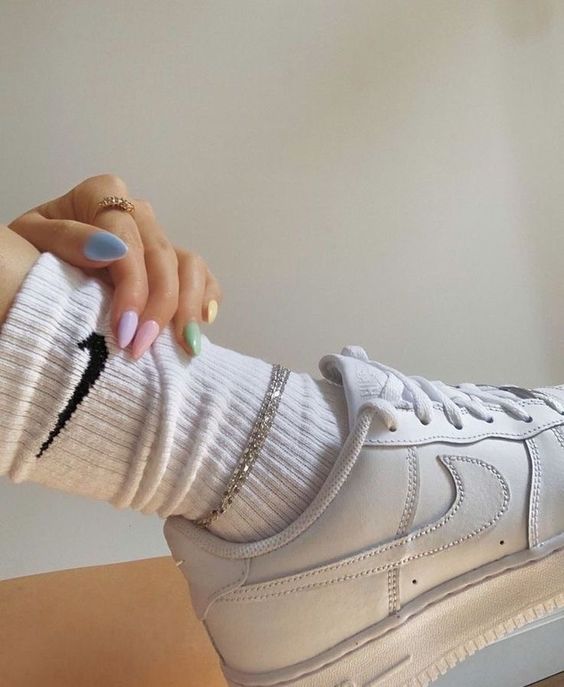 pies de chica con calcetas y tenis blancos posando sus uñas de colores pastel