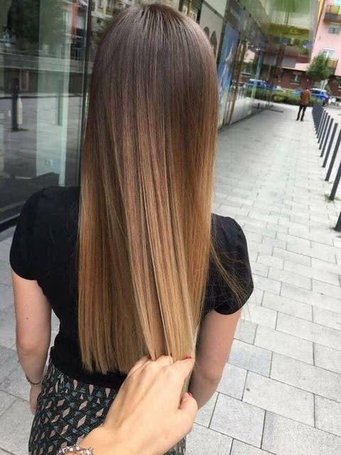 Mano tocando el cabello lacio y castaño de una chica que posa de espaldas con blusa negra