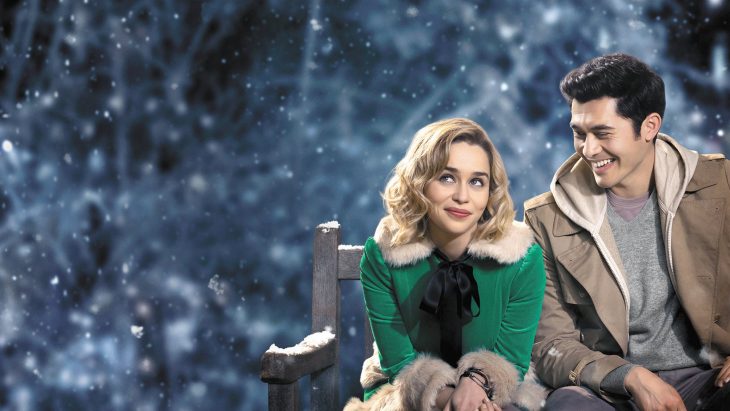 Emilia Clarke y Henry Golding sentados en una banca mientras actúan en la película Last Christmas