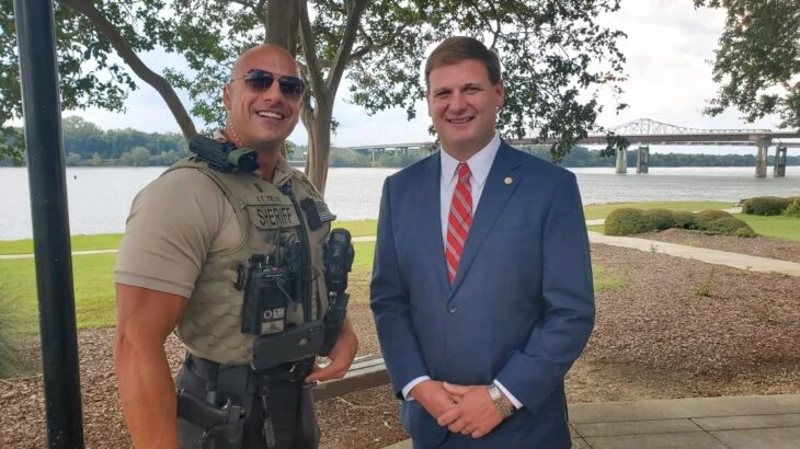 Policía junto a un hombre con traje; policía de Alabama que es un clon exacto de Dwayne Johnson