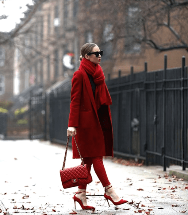 mujer de cabello claro con bufanda roja gruesa, top rojo, pantalones ajustados rojos, abrigo rojo largo, bolso de mano rojo y zapatos de tacón rojos
