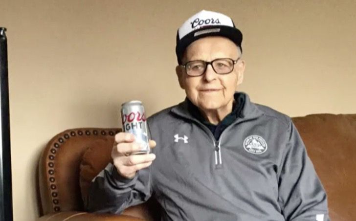 Andrew Slavonic sentado en un sillón vistiendo una sudadera gris y sosteniendo una cerveza Coors Light en la mano derecha
