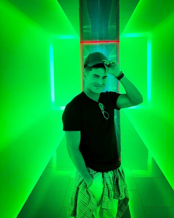 Zac Efron posando para una fotografía en un cuarto verde