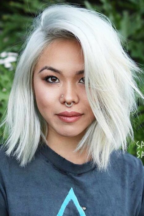Chica asiática con cabello corto en capas en color blanco 'icy blond' vistiendo blusa azul marino y con septum en la nariz