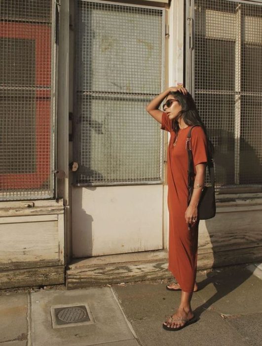 Mujer se toca el cabello y usa vestido naranja largo y flip flops