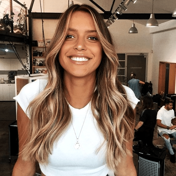 chica morena con cabello money piece de color castaño y mechas rubias al frente, camiseta blanca y collar plateado
